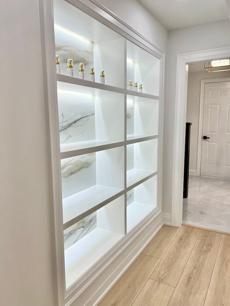 Built-in white product display shelf with luxurious Calacatta marble tile backsplash at Lash Layer & Brow Boutique in Pickering, Ontario.