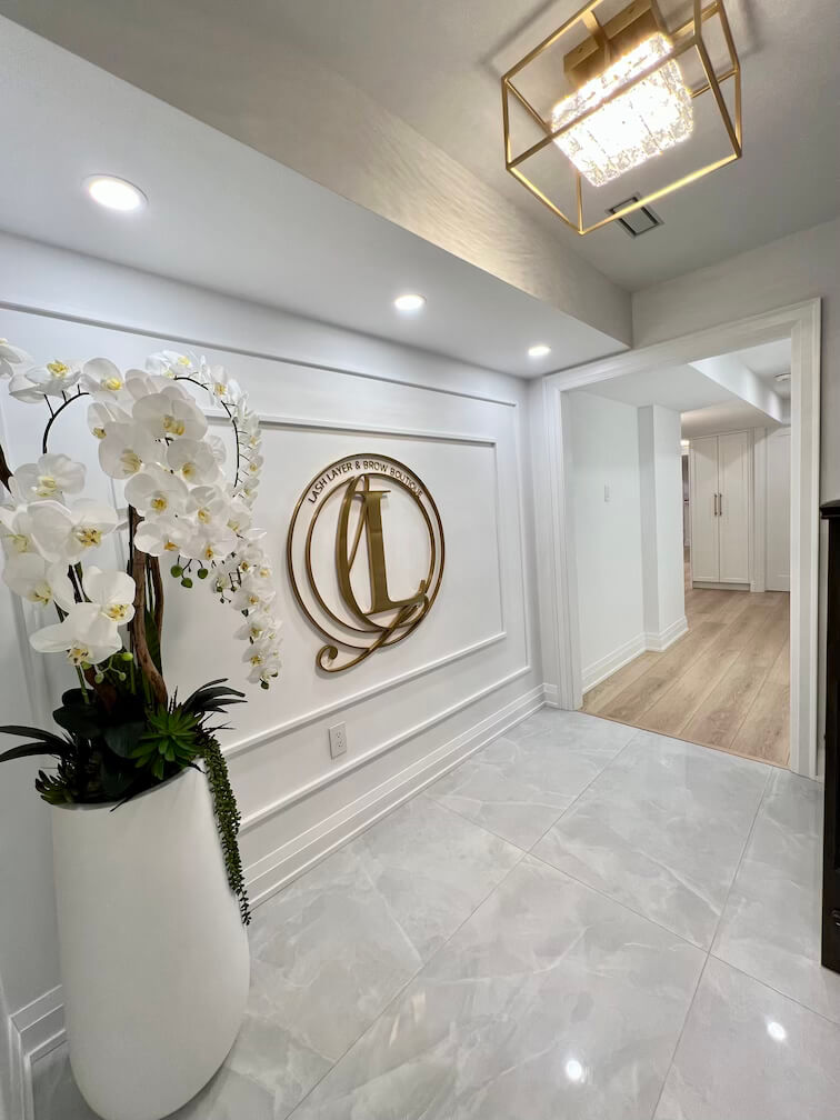 Elegant entrance of Lash Layer & Brow Boutique in Pickering, Ontario – featuring a gold logo, white orchids, and modern luxury décor.